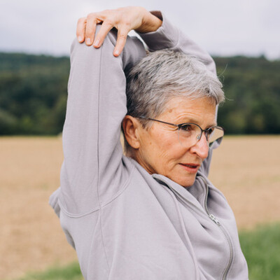 personalized lymphatic support, older woman stretching while standing up outside